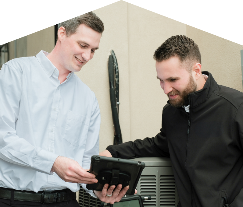A Moore & Russell technician in a white shirt shows service details on a tablet to a smiling client in a black jacket, standing beside an AC unit outside a beige building. A Moore & Russell technician in a white shirt shows service details on a tablet to a smiling client in a black jacket, standing beside an AC unit outside a beige building.