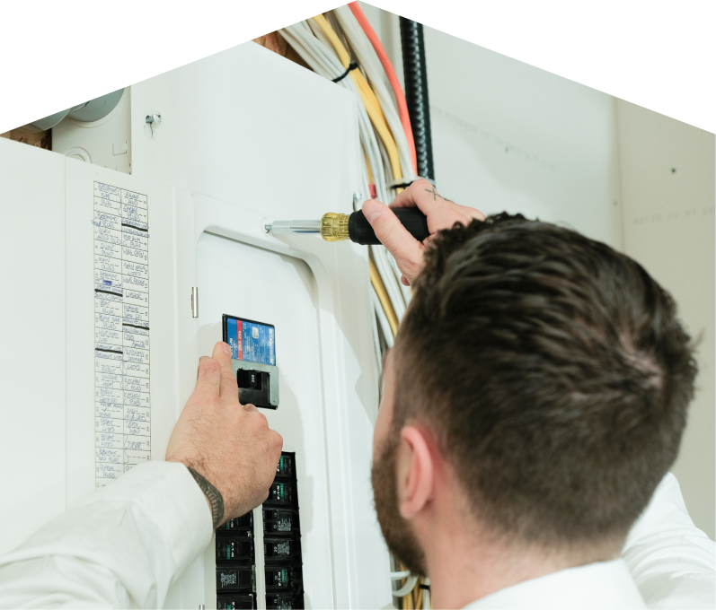 Moore & Russell electrician using a screwdriver to perform an electrical panel upgrade, working near organized wiring in a residential wall. Moore & Russell electrician using a screwdriver to perform an electrical panel upgrade, working near organized wiring in a residential wall.