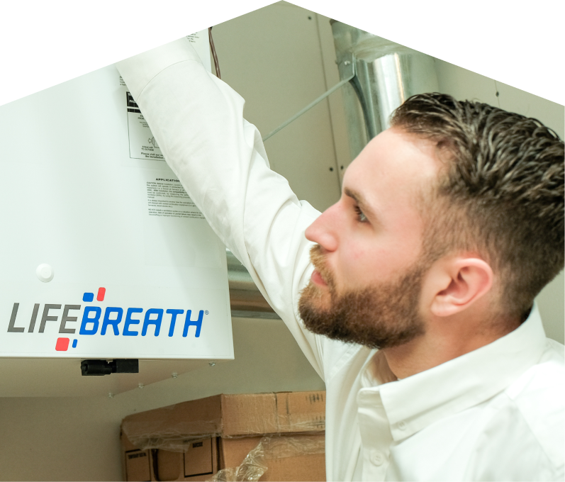 Moore & Russell indoor air quality specialist inspects a Lifebreath ventilation unit related to UV air purifiers, with ductwork and boxes in the background. Moore & Russell indoor air quality specialist inspects a Lifebreath ventilation unit related to UV air purifiers, with ductwork and boxes in the background.