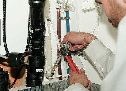 Using two pipe wrenches, a Moore & Russell professional plumber services a pipe connection near a vertical flue or vent pipe. Using two pipe wrenches, a Moore & Russell professional plumber services a pipe connection near a vertical flue or vent pipe.